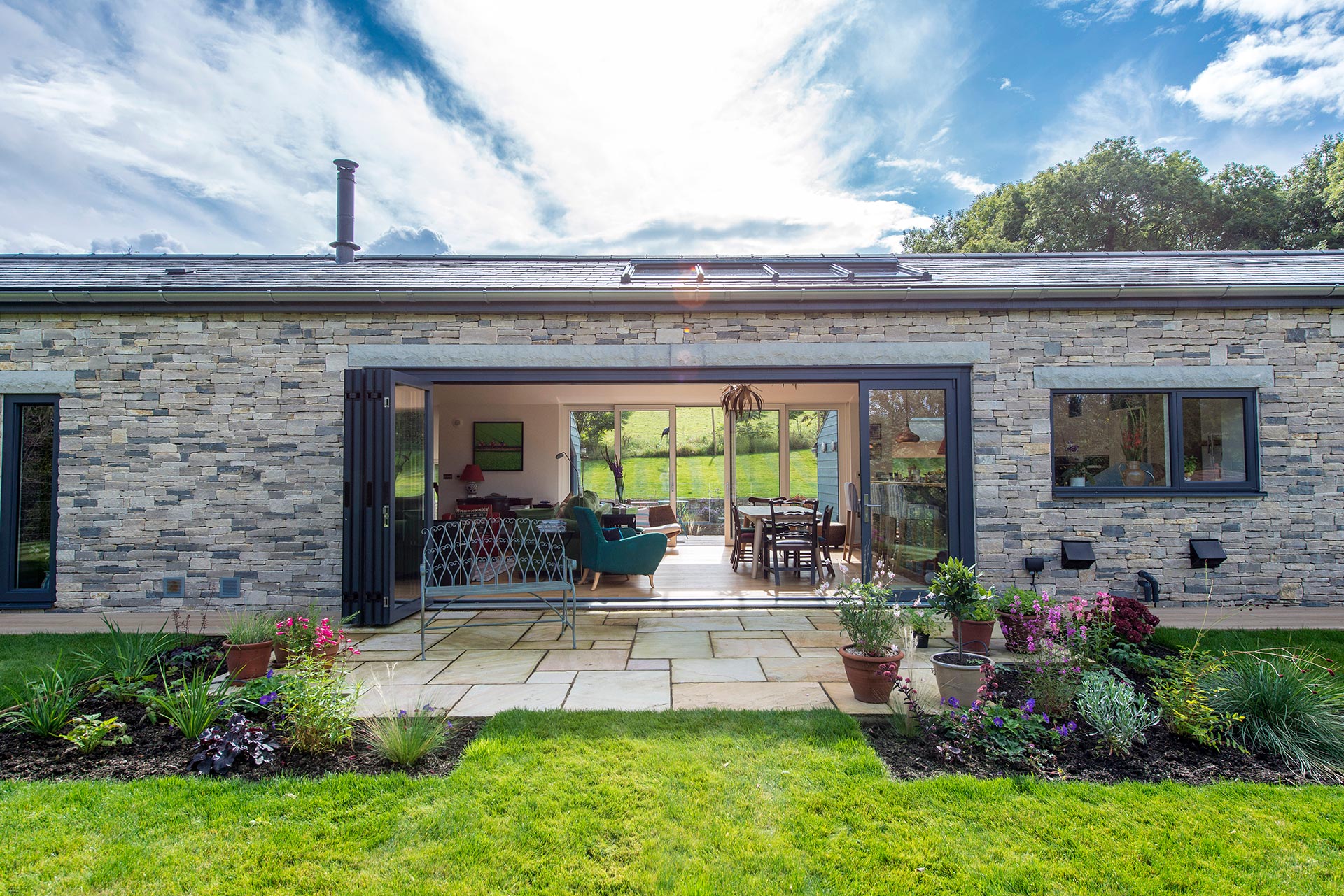 single storey stone house with large glass sliding doors leading onto patio and lawn garden