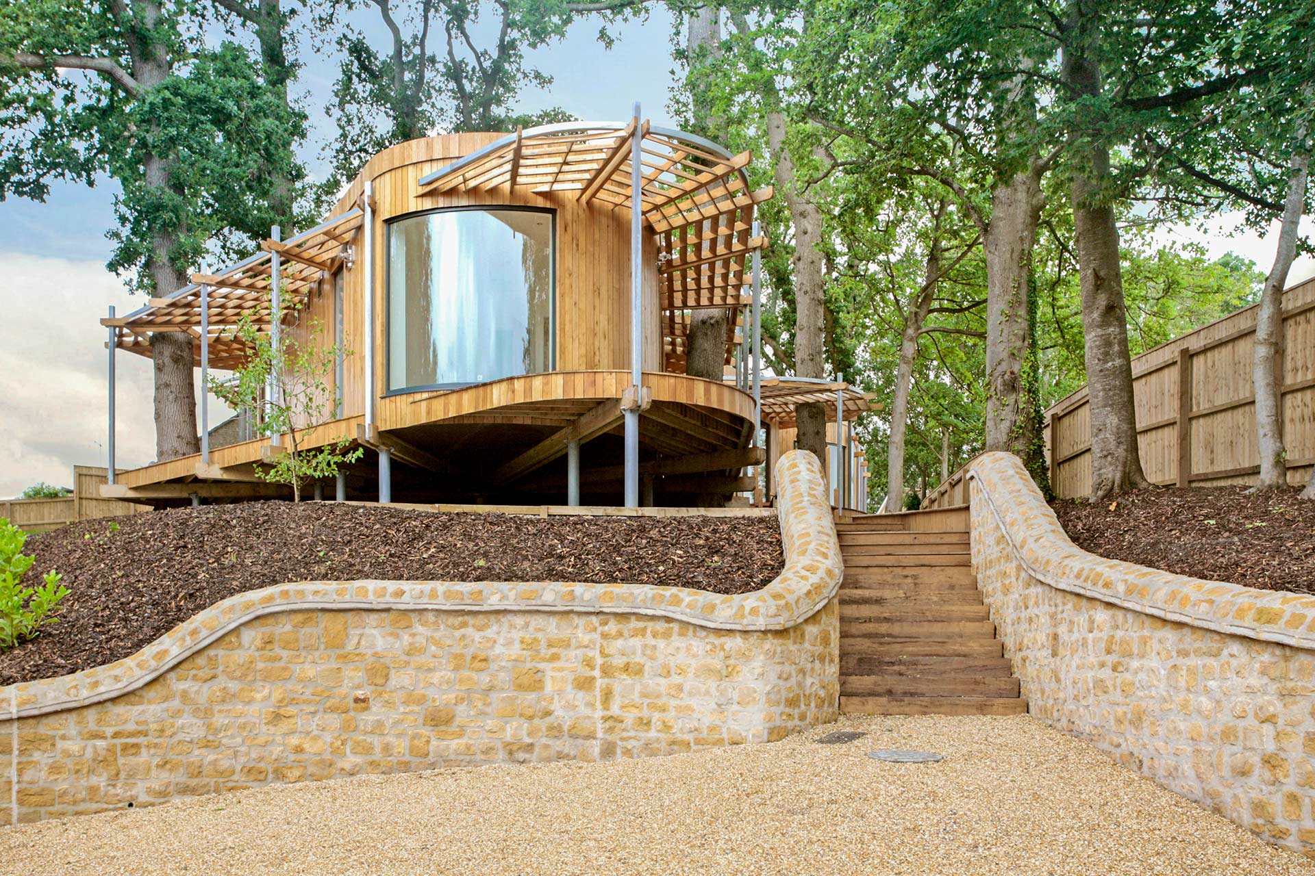 front view of timber cladded house in pod style surrounded by trees from driveway